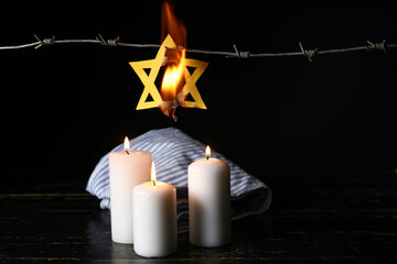 Prisoner uniform, burning Star of David, glowing candles and barbed wire on dark background....