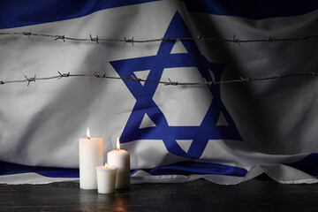 Burning candles with barbed wire and large flag of Israel on dark background. Holocaust Remembrance...
