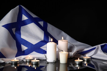 Burning candles with barbed wire and large flag of Israel on dark background. Holocaust Remembrance...