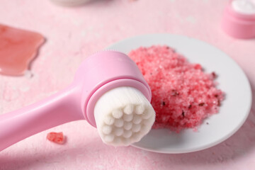 Facial massage brush and saucer with sea salt on pink background, closeup