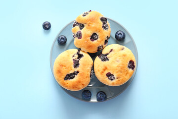 Plate with tasty blueberry muffins on blue background