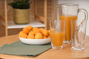 Jug of juice and bowl with apricots on coffee table in room. Closeup