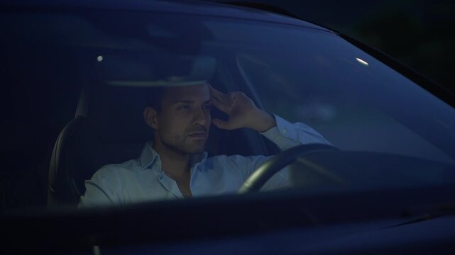 A contemplative man is sitting in his car during a quiet night, deep in thought and reflection