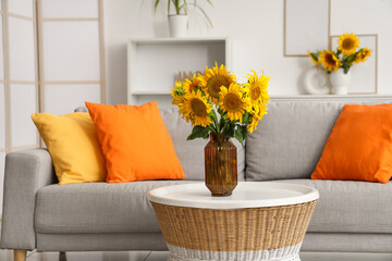 Stylish living room with grey sofa and vases of sunflowers bouquets on coffee table