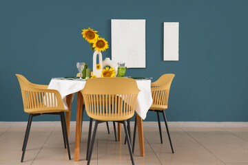 Modern table setting with sunflowers in vase near blue wall in room