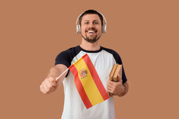 Handsome man in headphones with flag of Spain and books on brown background