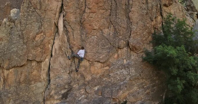 Young rock climber on side of rocky mountain at sunrise - drone shot growing wider