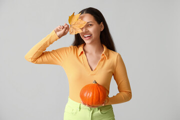 Stylish young woman with fresh pumpkin and autumn leaf on grey background