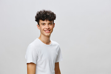 Young man with curly hair smiling against a light grey background, wearing a plain white t shirt, embodying joy and positivity in a minimalistic setting