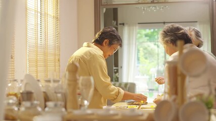 Group of Happy Asian senior women having breakfast together at home. Elderly retired woman friends enjoy healthy lifestyle making homemade greek yogurt with mixed fruit, nuts and honey in the kitchen.
