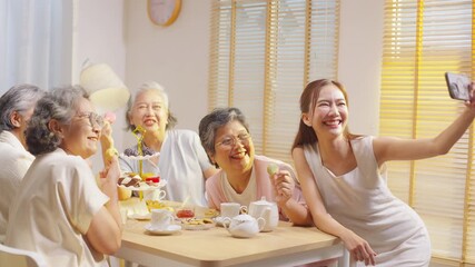 Group of Happy Asian senior women having meeting party afternoon tea at home. Daughter using mobile phone taking selfie with elderly retired mother and friends during drinking tea and eating bakery