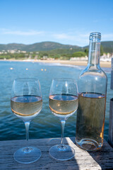 Bottle and glass of cold rose wine from Provence and wooden yacht boota pier on white sandy beach Plage de Pampelonne near Saint-Tropez, summer vacation in France