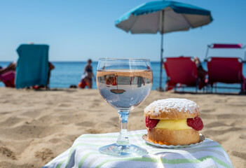 Lunch on sandy beach in Saint-Tropez with cake Tarte tropezienne filled brioche with cream and fresh red berries and glass of rose wine, summer vacation on French riviera, France
