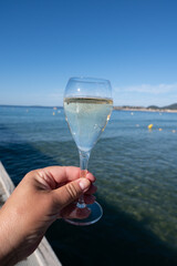 Summer time in Provence, hand with glass of cold champagne cremant sparkling wine on famous Pampelonne sandy beach near Saint-Tropez in sunny day, Var department, France, beach club party