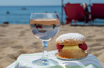 Lunch on sandy beach in Saint-Tropez with cake Tarte tropezienne filled brioche with cream and fresh red berries and glass of rose wine, summer vacation on French riviera, France