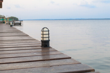 Wooden bridge with floor lights over river bank warm sunlight in evening. Morning seascape nature background.