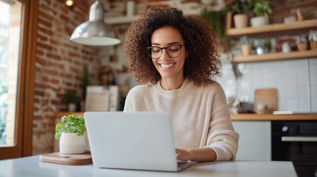 A happy woman is working on her laptop in a modern and cozy kitchen, showcasing a balanced and cheerful remote working environment in a beautifully decorated space.