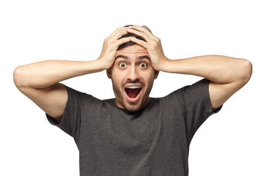 Emotional young man with round eyes, open mouth and hands pressed to top of head, showing astonishment and shock
