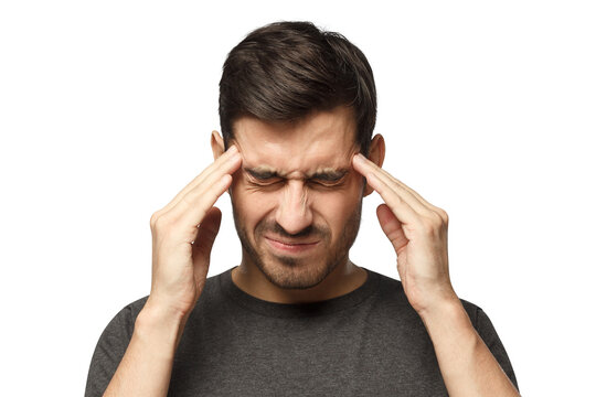 Portrait of young man suffering from severe headache, pressing fingers to temples with closed eyes