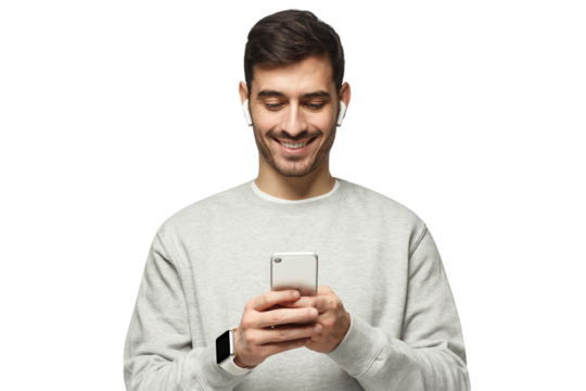 Young man standing, wearing wireless earphones, looking at screen of phone with smile, typing or surfing online