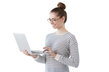 Indoor photo of positive teenage girl standing with laptop, smiling at great content from social networks, pressing fingers to touchpad in order to browse web pages