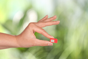 Woman with SIM card against blurred green background, closeup