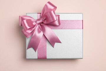 Beautiful gift box with pink bow on beige background, top view