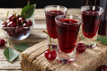 Shot glasses of delicious cherry liqueur and juicy berries on wooden table, closeup