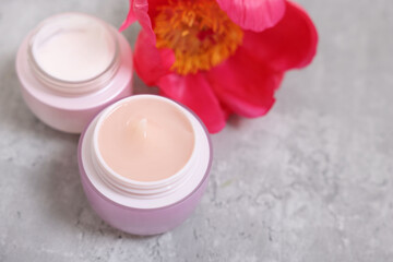 Jars of creams and peony flower on gray table. Space for text