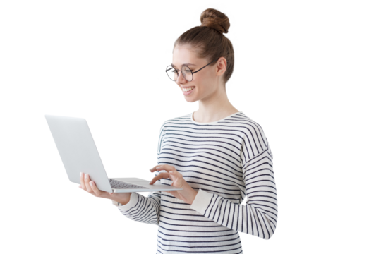 Indoor photo of positive teenage girl standing with laptop, smiling at great content from social networks, pressing fingers to touchpad in order to browse web pages