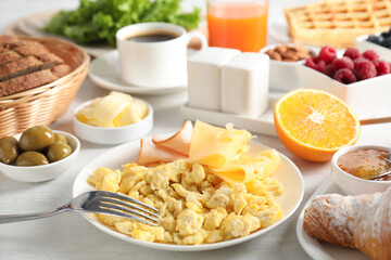 Tasty breakfast. Scrambled eggs, ham, cheese and other food served on light table, closeup