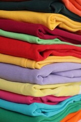 Stack of clean colorful t-shirts as background, closeup