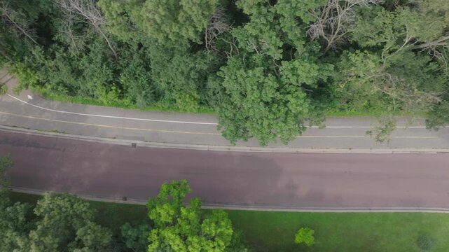 Drone view of a cyclist cycling through pathways between forest in St. Louis Park of Minnesota, USA.