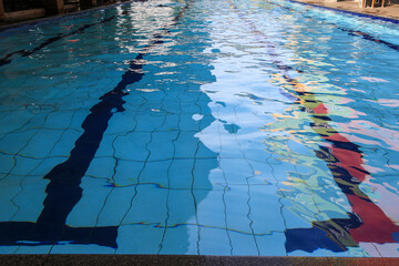Obraz premium A calm swimming pool with blue water and ripples on the surface. Swimming Pool with Ripples. A clear blue swimming pool with a black line in the middle The water is rippling and reflecting the light