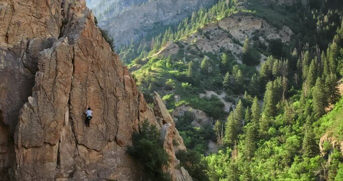 Cinematic drone shot of rock climbing high on rocky mountain at sunrise - aerial shot