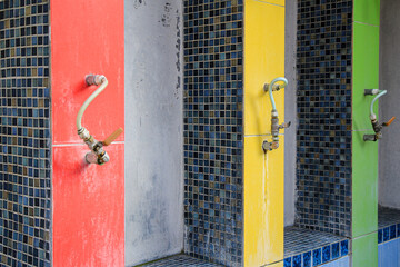 Close-up of a colorful tiled wall with multiple faucets, in a bathroom or public space. Colorful tile wall with three outdoor faucets.