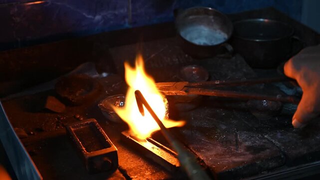 Goldsmith heats a metal rod with tongs over an open flame in a workshop, shaping the glowing metal
