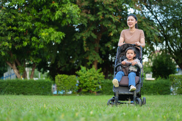 happy mother pushing toddler baby stroller and walking in park