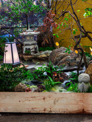 Minimal Japanese garden in home with small stone lantern and bamboo fountain and moss and flowers.
