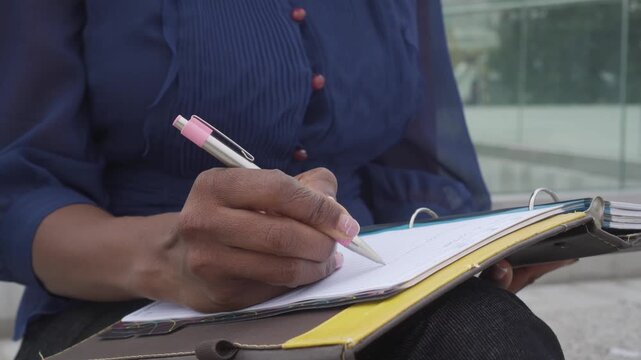 close up of a female Afro student's hands writing in a notebook