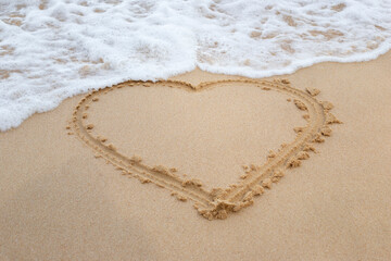 Hand drawing heart on sand and fleeing wave on beach. A heart-shaped symbol drawn on the sandy shore by the sea. A fleeing wave of the sea next to a heart painted on the sand