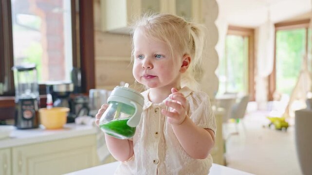 Little Girl Drinks Green Juice in the Kitchen