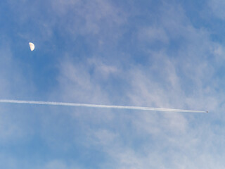 Plane flies pass over the moon on blue sky airplane trail