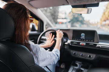 A woman sits in the driver's seat of a car, gripping the steering wheel with one hand, focused on the road ahead