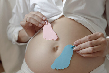 pregnant woman holding card with boy or girl decoratoin feet, gender reveal surprise party