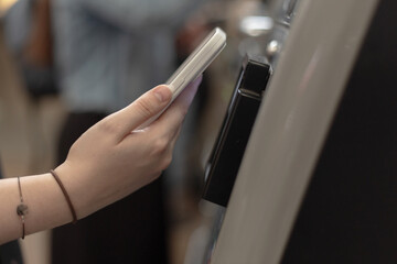Female hand with mobile phone to pay at self-service terminal