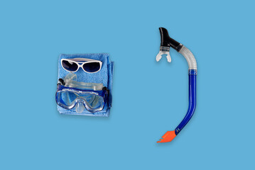 Items for diving and swimming on blue background: snorkeling breathing tube, plastic glasses and...