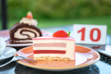 A slice of cake with a strawberry on top sits on a plate next to a sign that say