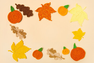 Autumn frame made of knitted toys in the shape of oak and maple leaves, orange pumpkins on a beige background with a place for text in the middle. Concept of autumn, Thanksgiving, Halloween