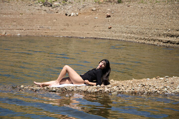 beautiful young brunette latin woman in black shirt and black bikini lying relaxed on the shore of...